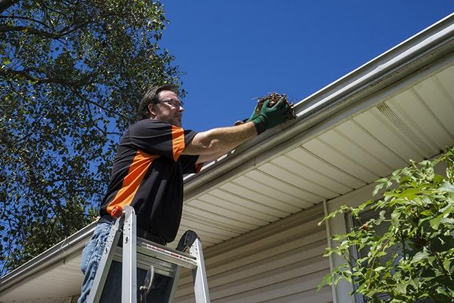 a worker inspecting and repairing a clogged gutter in Columbus Junction